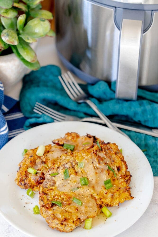 breaded chicken fried steak on a white plate in front of an air fryer 