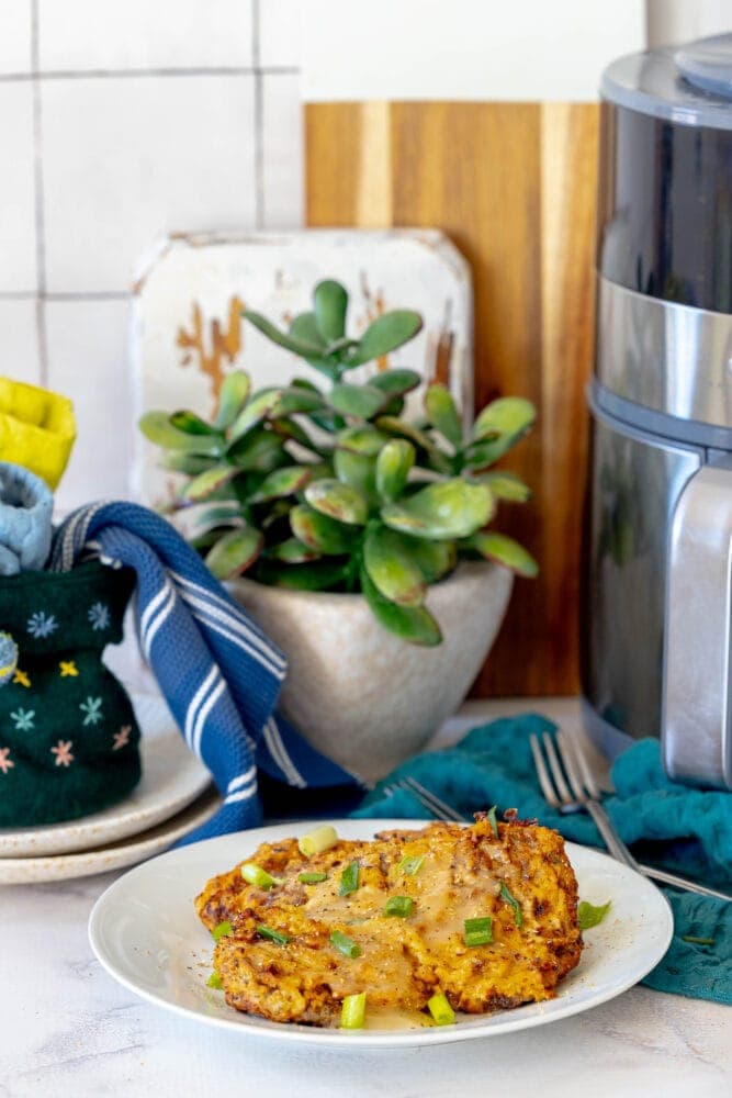  breaded chicken fried steak on a white plate in front of an air fryer 
