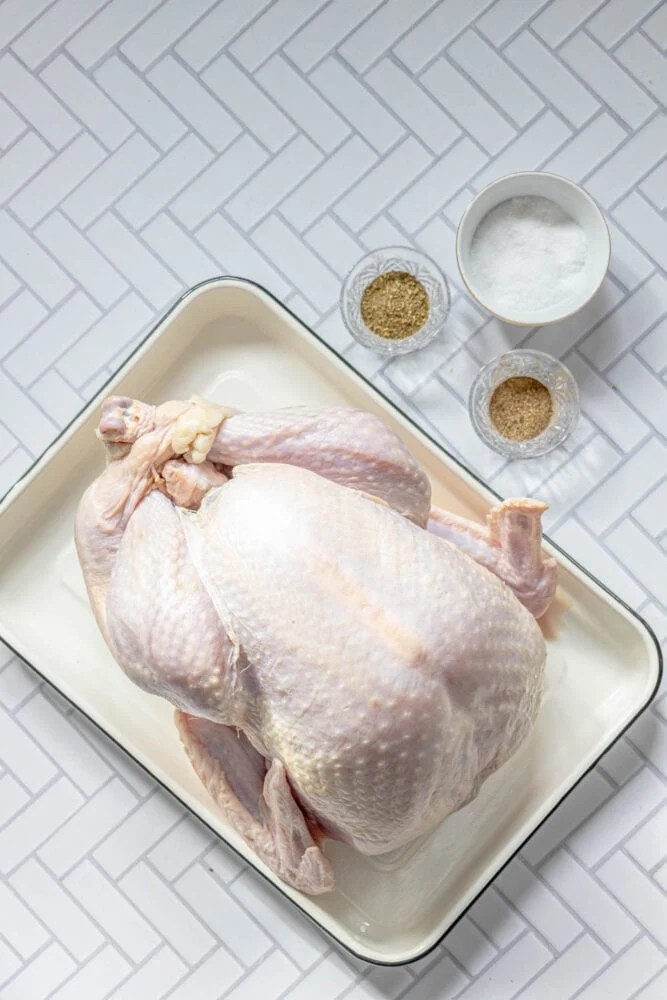 picture of turkey on a tray next to salt, pepper, and herbs