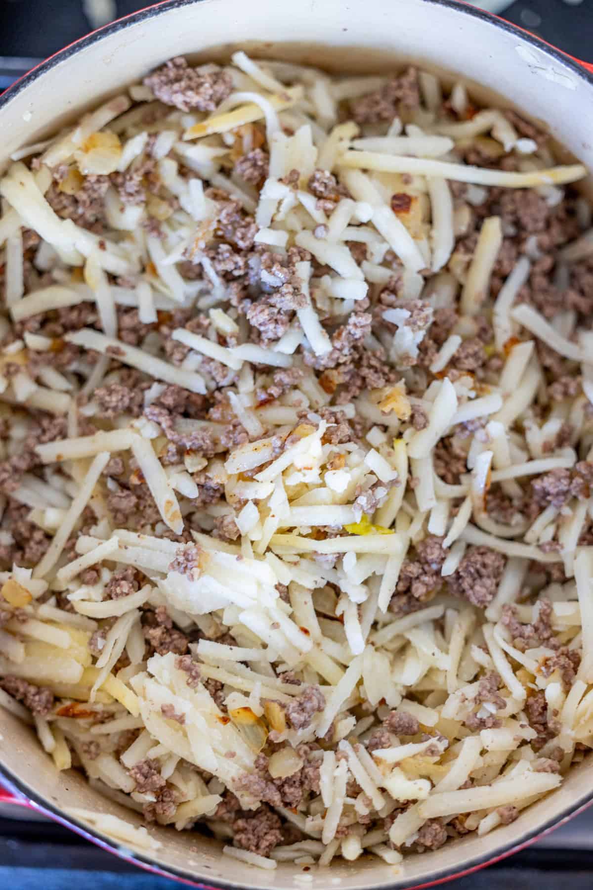 A pot filled with creamy hash brown hamburger soup, featuring cooked ground beef and shredded potatoes.