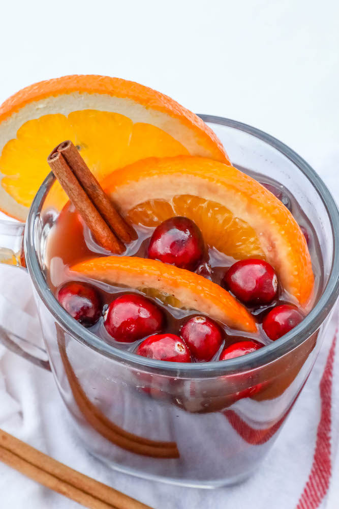 cider in a clear mug with slices of orange and cranberries with cinnamon sticks