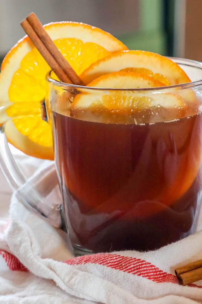 cider in a clear mug with slices of orange and cranberries with cinnamon sticks